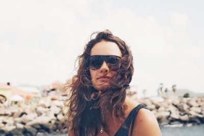 Close-up portrait of young woman wearing sunglasses against sky