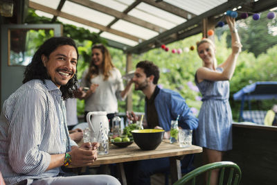 Portrait of happy man sitting at table while enjoying party with friends at summer house