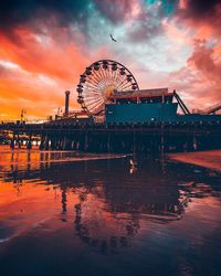 Ferris wheel by pier against sky during sunset