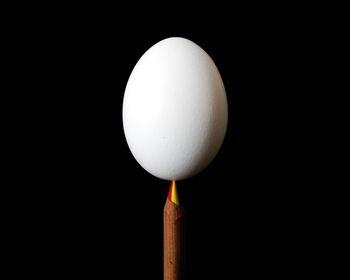 Close-up of white egg balancing on pencil against black background