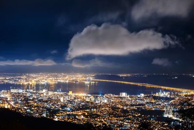 Illuminated cityscape by sea against sky at night