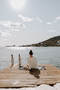 Rear view of woman sitting on pier by sea