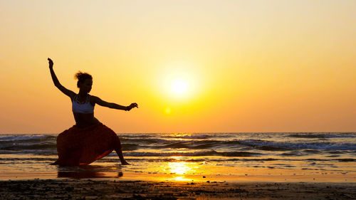 Woman dancing on beach against sky during sunset