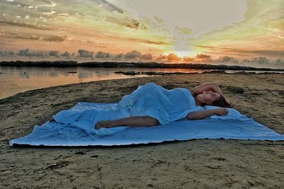Man lying down on beach against sky during sunset
