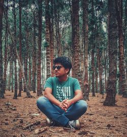 Young man sitting on tree trunk in forest