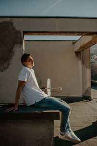 Side view of a man sitting against built structure