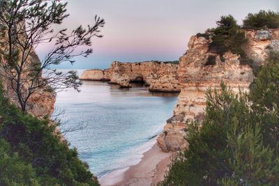 Rock formations in sea at praia da marinha during sunset