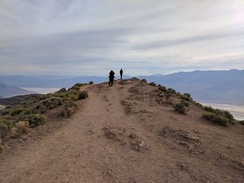 Rear view of people walking on mountain against sky