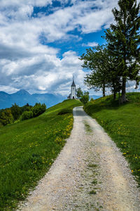Footpath leading towards trees against cloudy sky