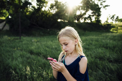 Girl using mobile phone while standing on grassy field
