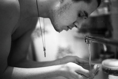 Shirtless young man washing hands in bathroom at home