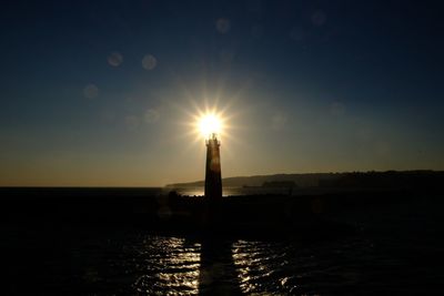 Sun shining over sea against sky during sunset