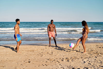 Multiethnic men and women playing beach ball on sandy beach near sea
