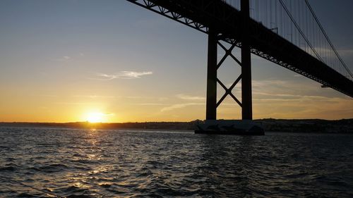 Silhouette bridge over sea against sky during sunset