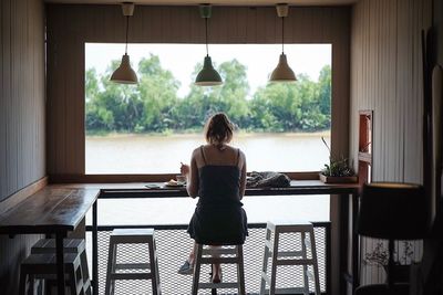 Rear view of woman sitting at table in restaurant against lake