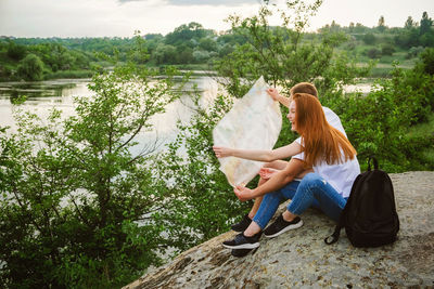 Woman sitting by lake against trees