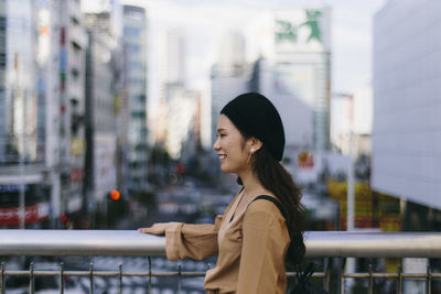 Side view of young woman standing against railing in city