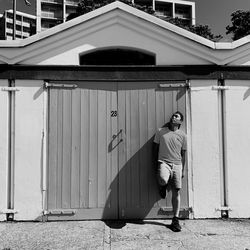 Full length of thoughtful man looking up while leaning on closed door during summer