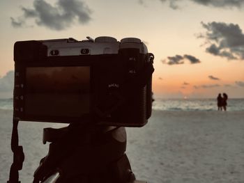 View of camera at beach against sky during sunset
