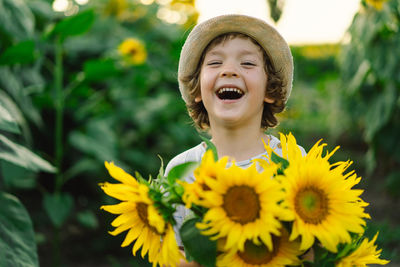 Happy boy walking in field of sunflowers. child playing with big flower and having fun.