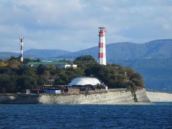 Lighthouse by building and mountains against sky