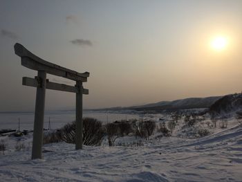 Torii gate on snow covered land against sky during sunset