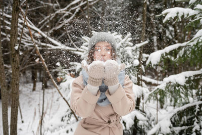 A cute girl in a hat and vazherzh holds snow in her hands and blows on it