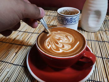 Cropped hand of man holding spoon in coffee at table