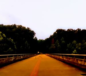 Empty road along trees and against clear sky