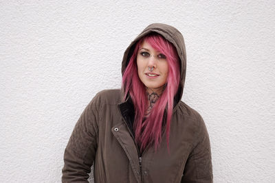 Portrait of young woman in pink hair standing against wall