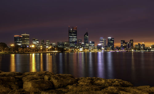 River by illuminated buildings against sky at night