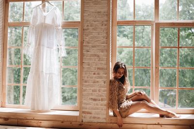 Woman sitting on window sill at home