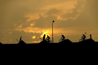 Silhouette of people cycling against sunset sky