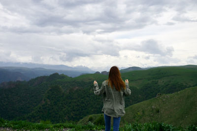 Rear view of woman standing on mountain against sky