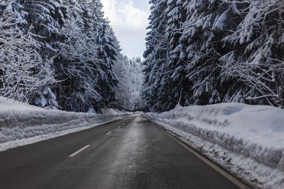 Road amidst snow covered trees against sky