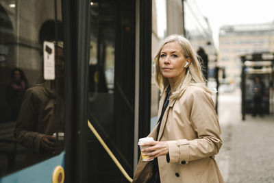 Businesswoman holding disposable cup while boarding bus in city