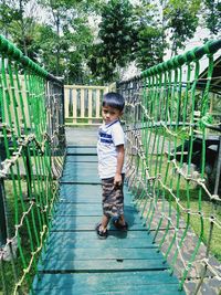 Portrait of boy standing on footbridge against trees