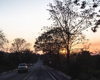 Silhouette of trees by road against clear sky