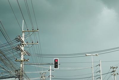 Low angle view of tangled cables by traffic signal against sky