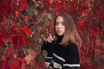 Autumn portrait of a beautiful cute woman against a background of bright red leaves. black sweater