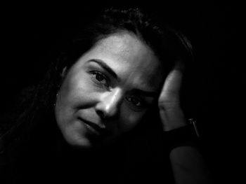 Close-up portrait of woman with hand in hair against black background