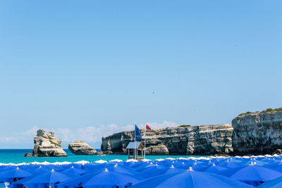 Rear view of buildings by sea against clear blue sky