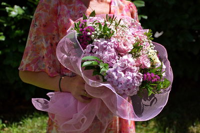 Midsection of mature woman in a park with bouquet of colorful flowers