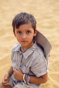 Portrait boy child traveler in a suit of an archaeologist and wearing hat sitting on sand in desert