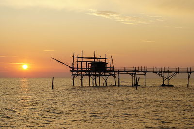 Silhouette cranes in sea against sky during sunset