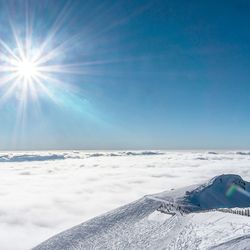 Scenic view of mountain with snow above clouds against clear sky with sun