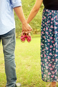 Low section of couple holding hands with baby booties while standing at park