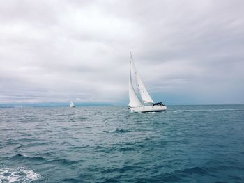 Sailboats sailing on sea against cloudy sky