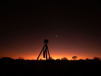 Silhouette of camera tripod standing against moody sky at dawn