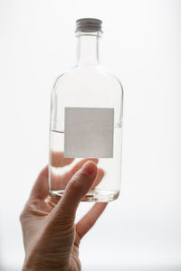 Close-up of hand holding glass bottle against white background